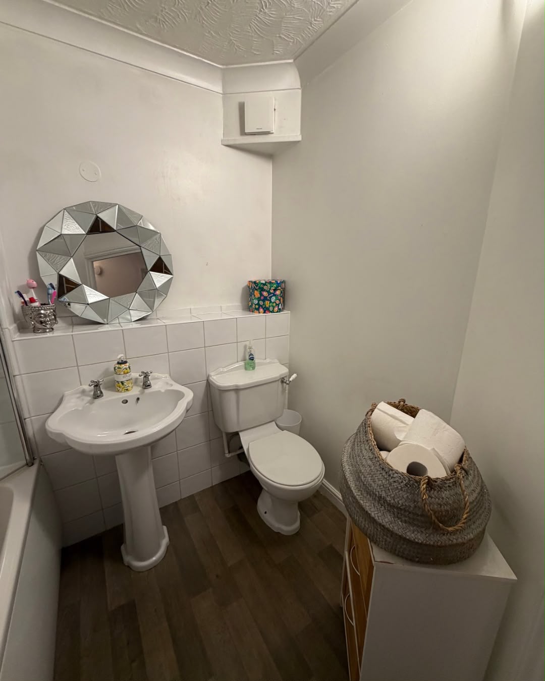 A cleaned bathroom with a white pedestal sink, toilet and geometric mirror