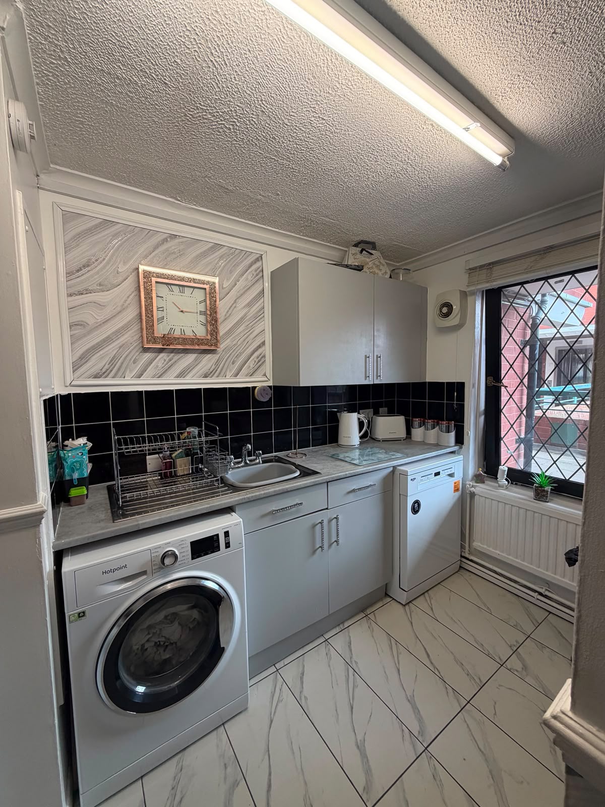 A cleaned galley kitchen and utility area with grey cabinets and a black tiled splashback