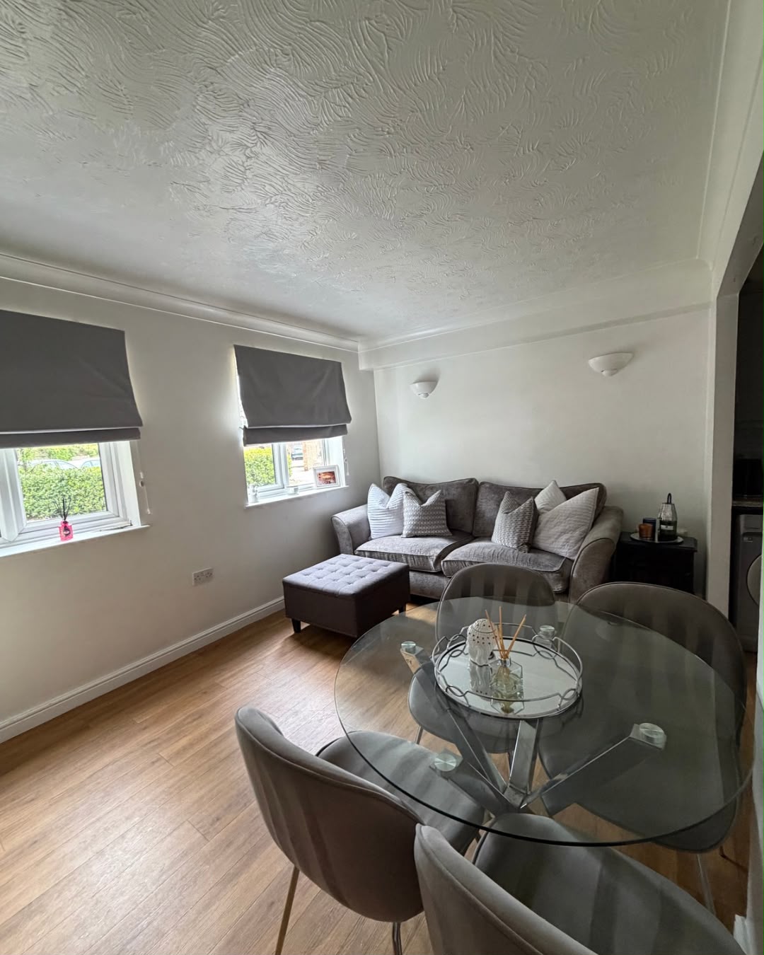 A tidied living and dining room with a grey sofa, glass dining table and wood-effect flooring